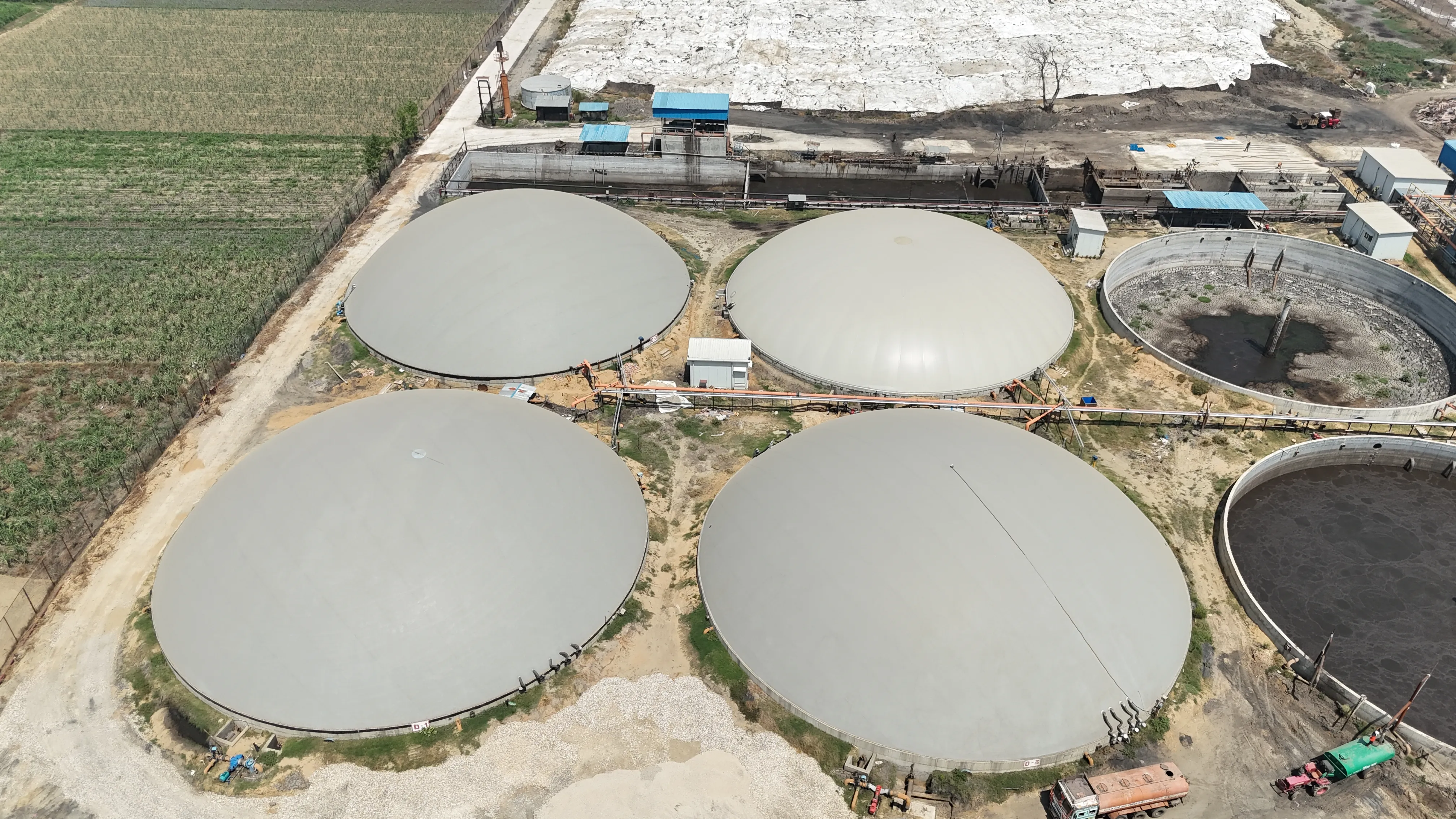 Overhead aerial of the four-digester bank at the Circle CBG Meerut plant, adjacent sugarcane field visible