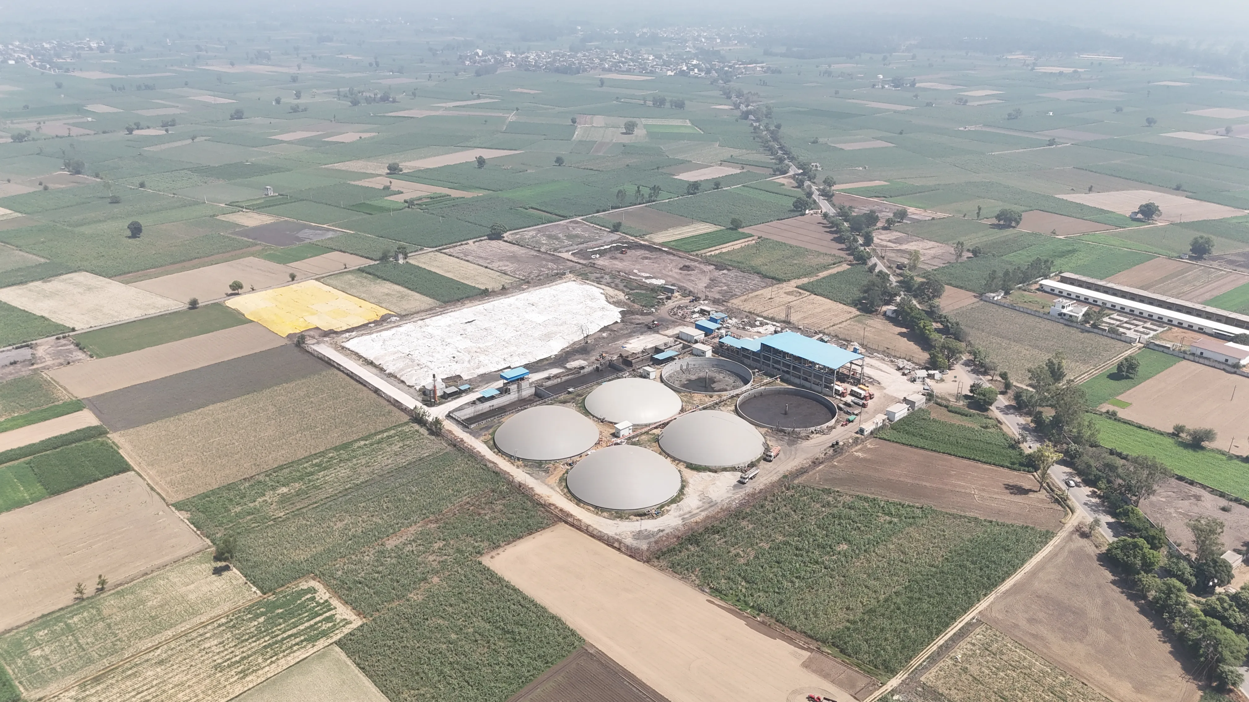 Wide aerial vista of the Circle CBG Meerut plant among farmland, with a village on the horizon